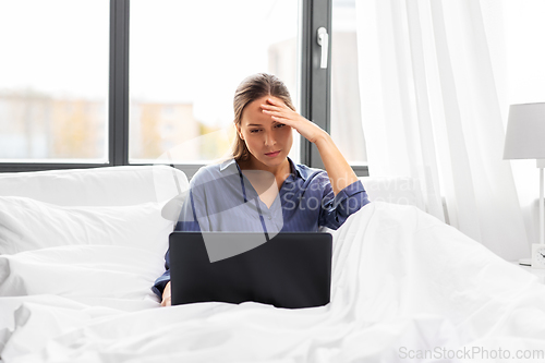 Image of stressed young woman with laptop in bed at home