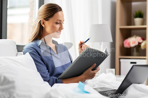 Image of young woman with laptop and papers in bed at home