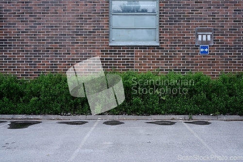 Image of empty parking near red brick wall and green bushes, deadpan phot