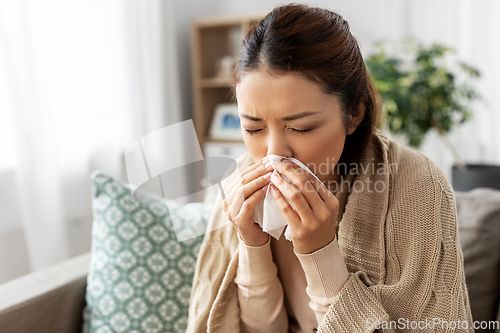 Image of sick woman blowing nose in paper tissue at home