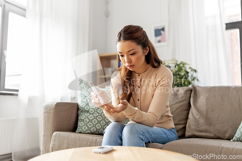 Image of asian woman making blood test with glucometer at home