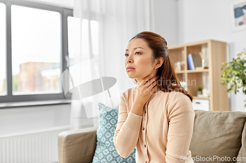 Image of sick asian woman touching her sore throat at home