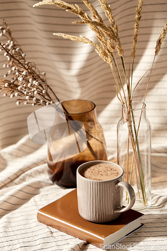 Image of cup of coffee on book and dried flowers in vases