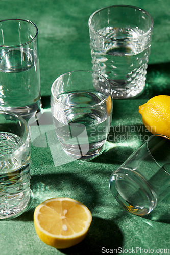 Image of glasses with water and lemons on green background