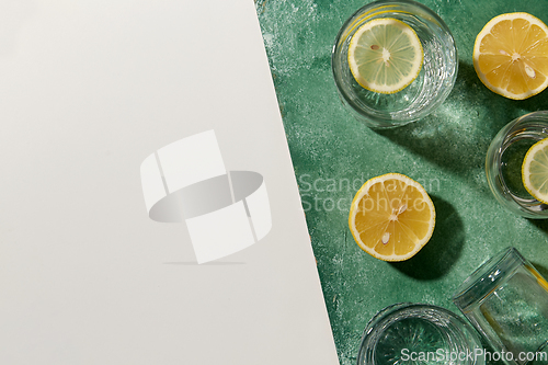 Image of glasses with water and lemons on green background