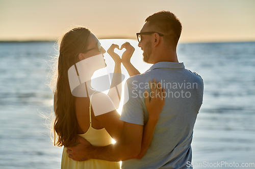 Image of happy couple showing hand heart on summer beach