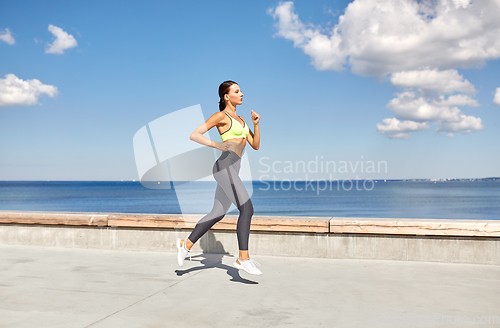 Image of young woman running along sea promenade