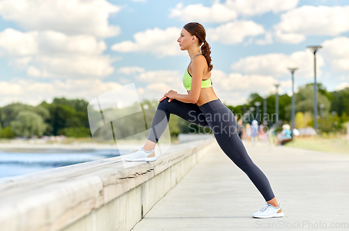 Image of happy young woman doing sports and stretching leg