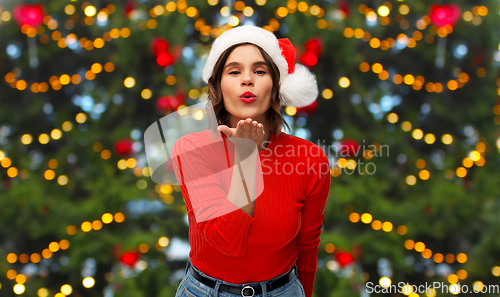 Image of happy young woman in santa hat sending air kiss