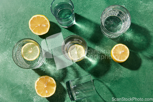 Image of glasses with water and lemons on green background