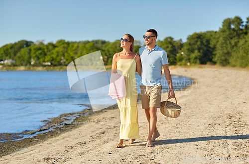 Image of happy couple with picnic basket walking on beach