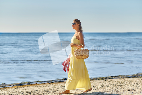 Image of happy woman with picnic basket walking along beach