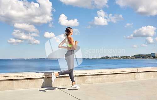 Image of young woman running along sea promenade