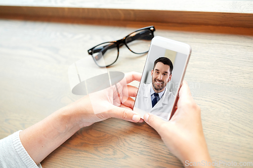 Image of hands of woman holding phone with doctor on screen