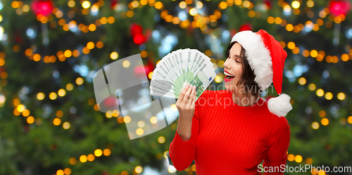 Image of happy woman in santa hat with money on christmas