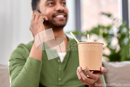 Image of man with takeaway food calling on phone at home