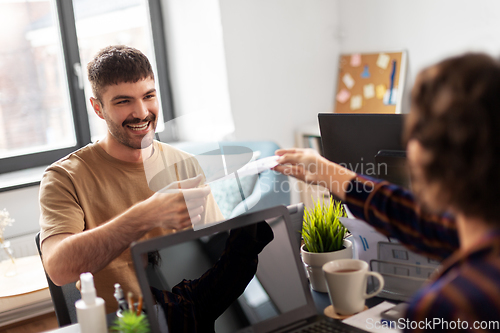 Image of smiling man taking papers from colleague at office