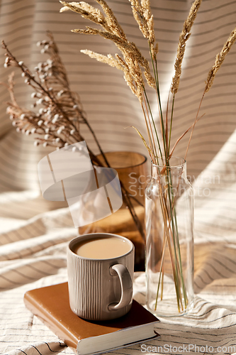 Image of cup of coffee on book and dried flowers in vases