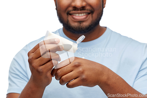 Image of happy african man applying moisturizer to his hand
