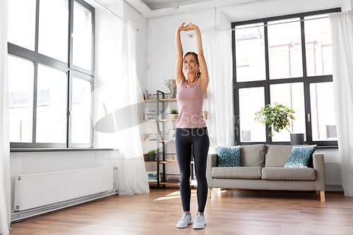 Image of smiling young woman stretching arms at home