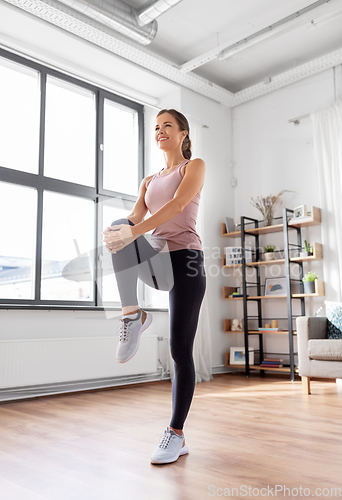 Image of smiling young woman stretching leg at home