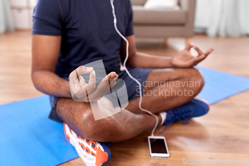 Image of indian man meditating in lotus pose at home