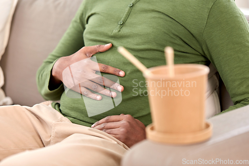 Image of close up of overeaten man and cup of takeaway food