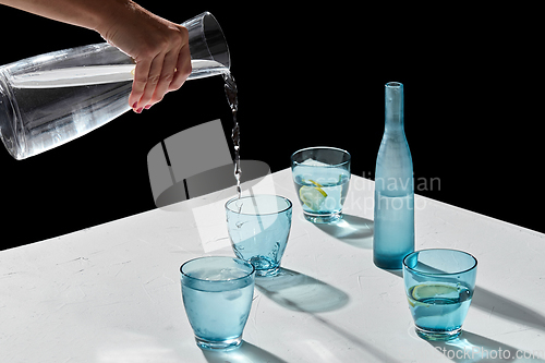 Image of hand pouring water to glasses with lemon and ice