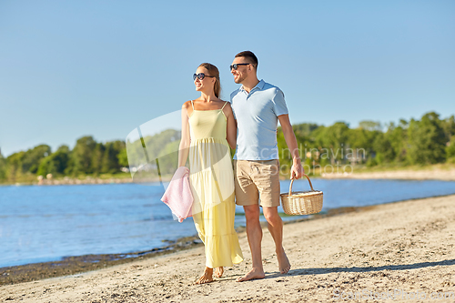 Image of happy couple with picnic basket walking on beach