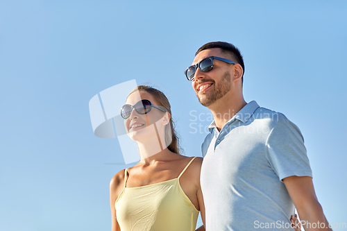 Image of happy couple in sunglasses hugging over blue sky