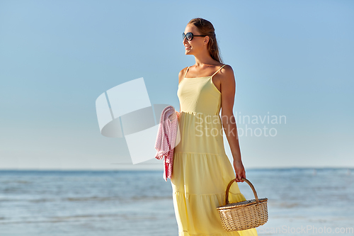 Image of happy woman with picnic basket walking along beach