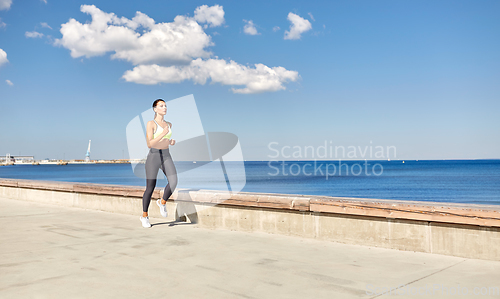 Image of young woman running along sea promenade