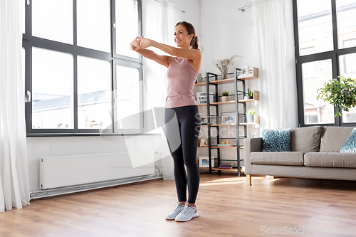 Image of smiling young woman stretching arms at home