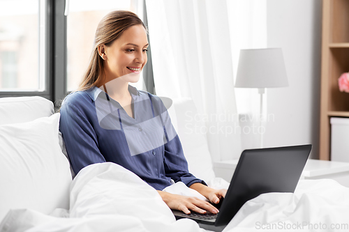 Image of young woman with laptop in bed at home bedroom