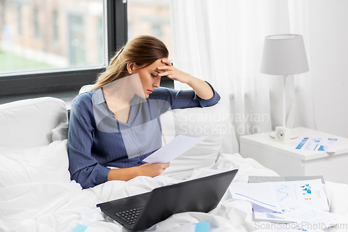 Image of young woman with laptop and papers in bed at home