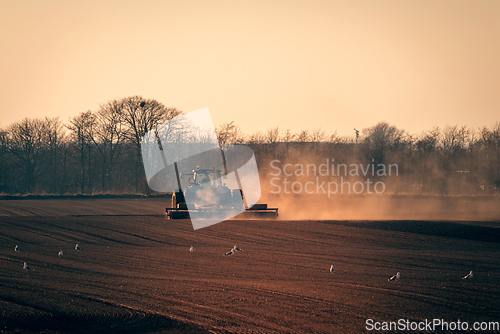 Image of Tractor on a field in the sun with dust flying