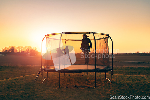 Image of Trampoline on a lawn in the sunset with two kids