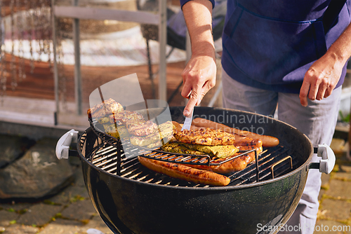 Image of Man by the barbeque with pork chops and sausages