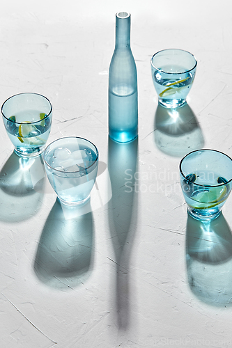 Image of glasses with water and lemons on white background