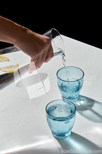 Image of hand pouring water to glasses with lemon and ice