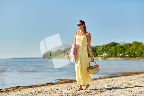 Image of happy woman with picnic basket walking along beach