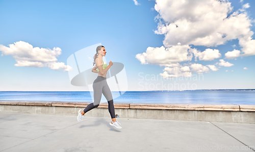 Image of young woman running along sea promenade