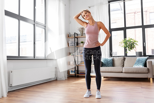 Image of smiling young woman stretching neck at home