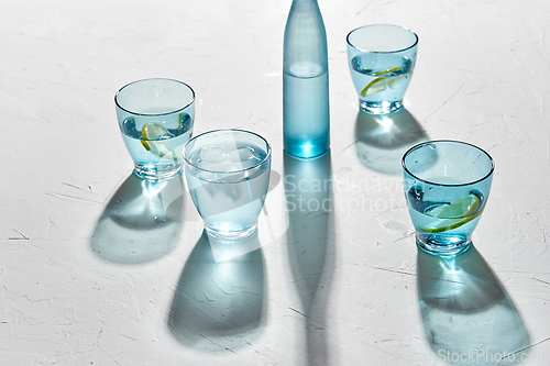 Image of glasses with water and lemons on white background