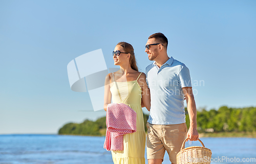 Image of happy couple with picnic basket walking on beach