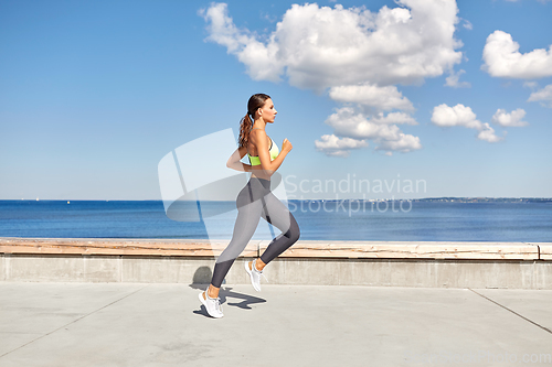 Image of young woman running along sea promenade