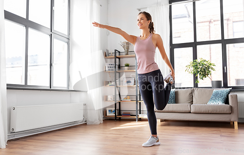 Image of smiling young woman stretching leg at home