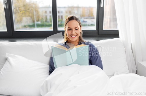 Image of young woman reading book in bed at home