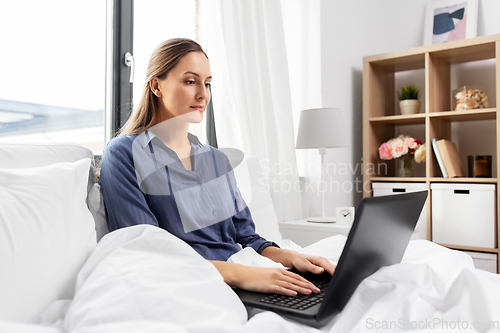 Image of young woman with laptop in bed at home bedroom