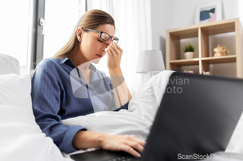 Image of tired woman in glasses with laptop in bed at home